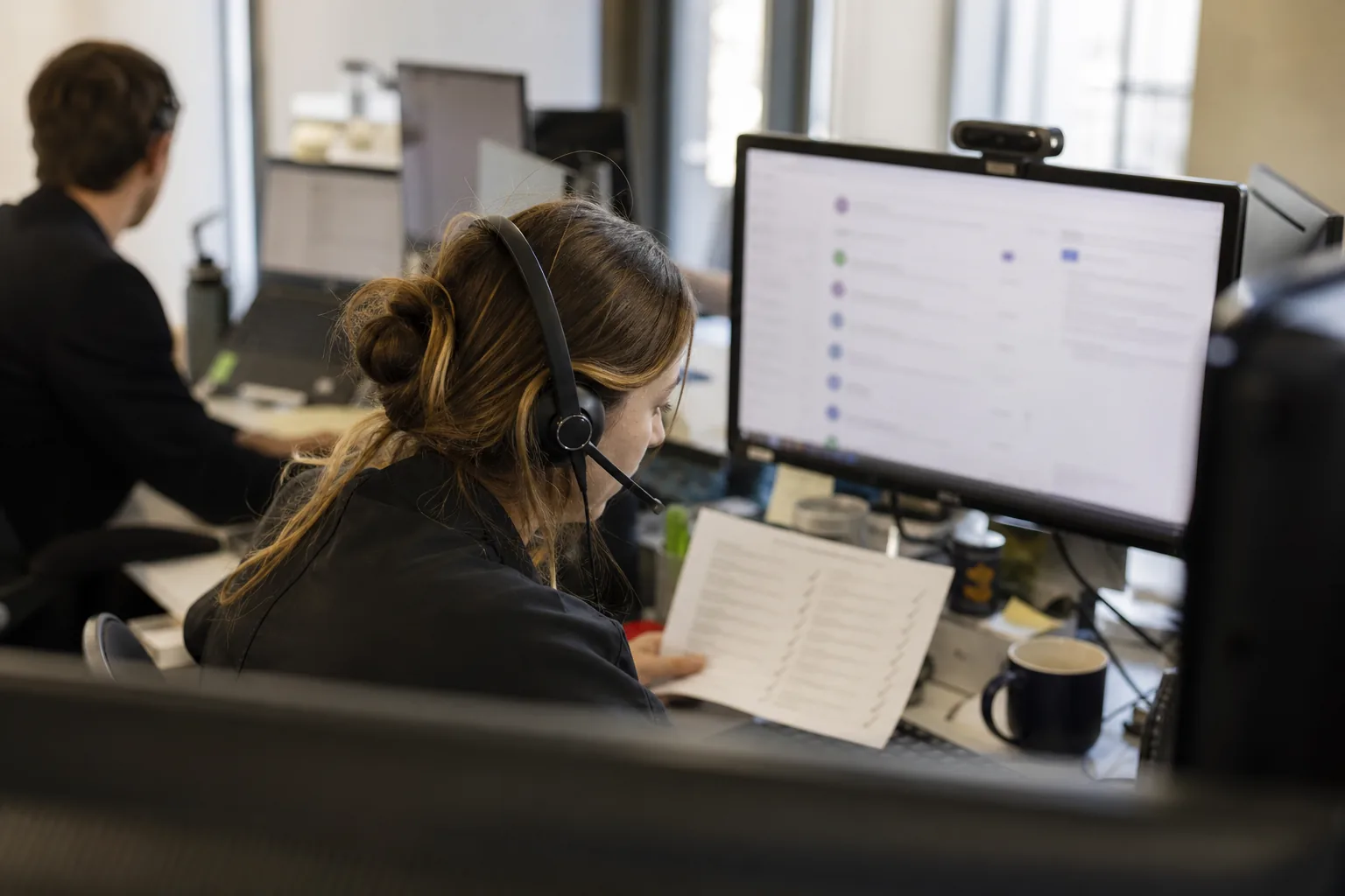 Sales rep with a headset working through a printed prospect list at a sales desk