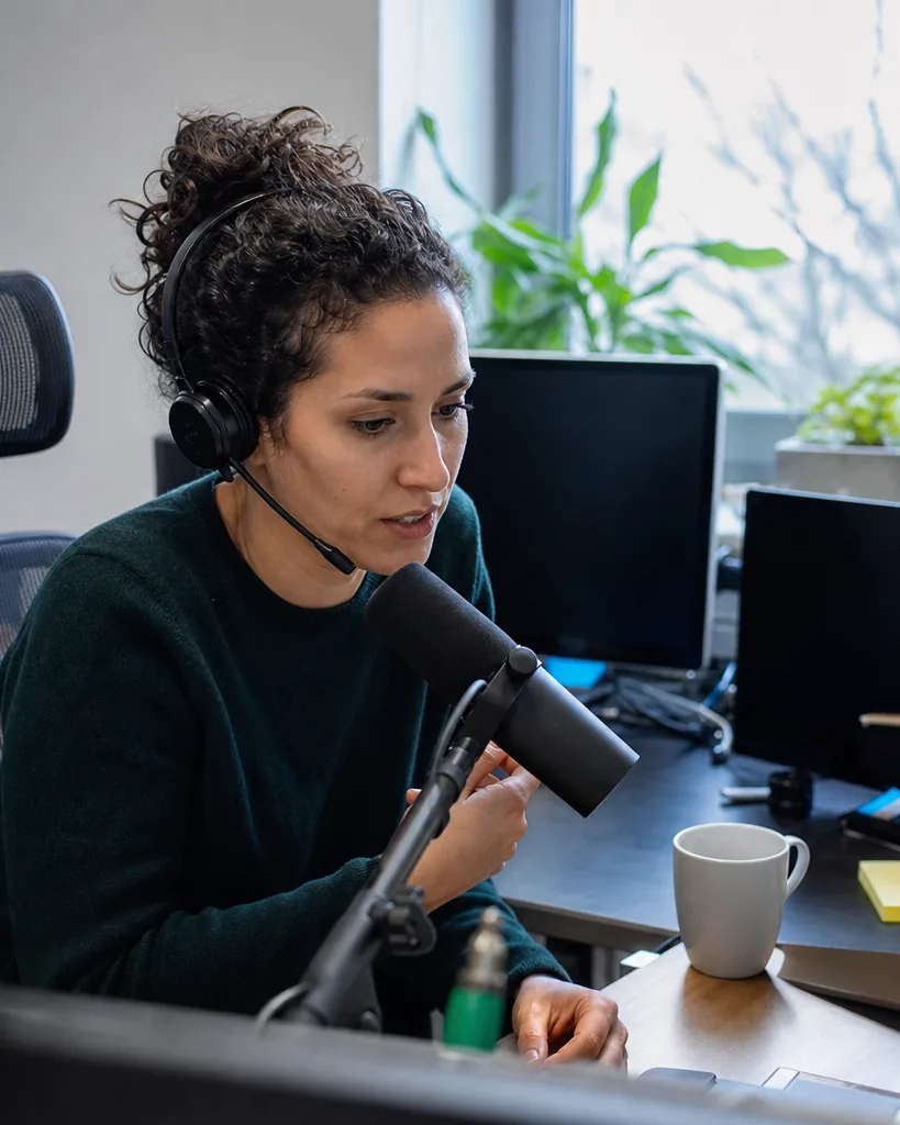 Support lead with a headset recording a short explainer at her desk, monitors switched off beside her